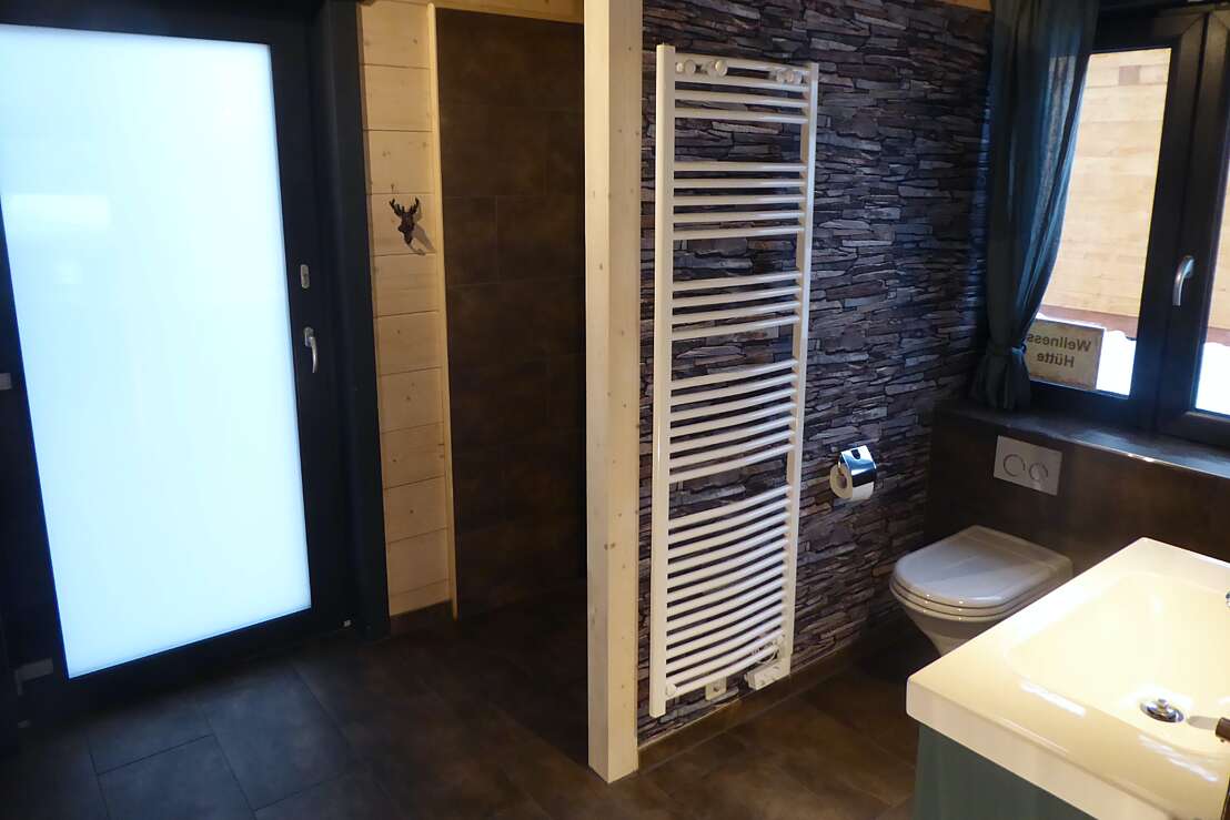 Badezimmer mit großzügiger, bodentiefer Dusche und Blockbohlen-Sauna